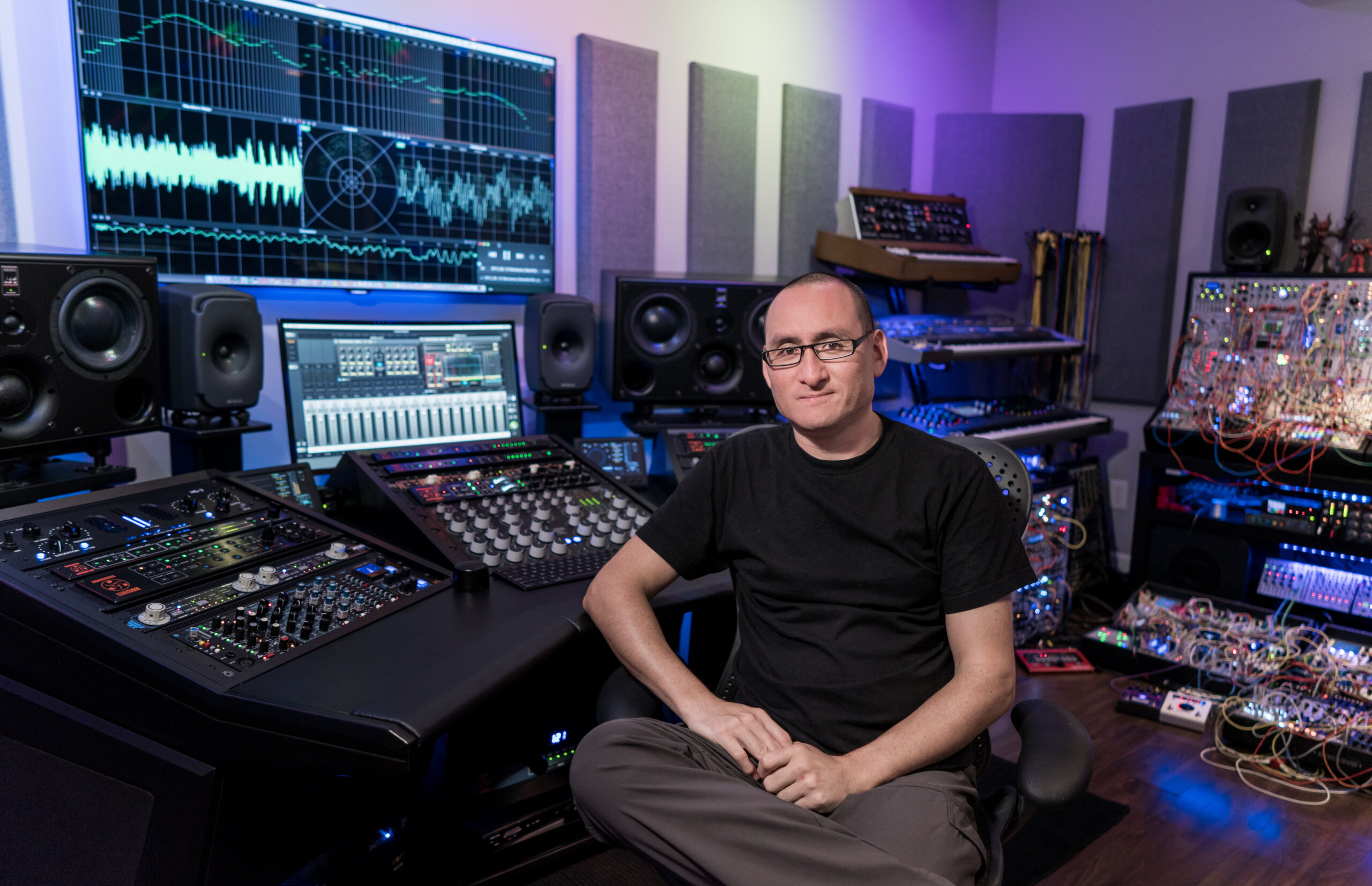 Richard Devine seated in his studio, surrounded by synthesizers and audio equipment.